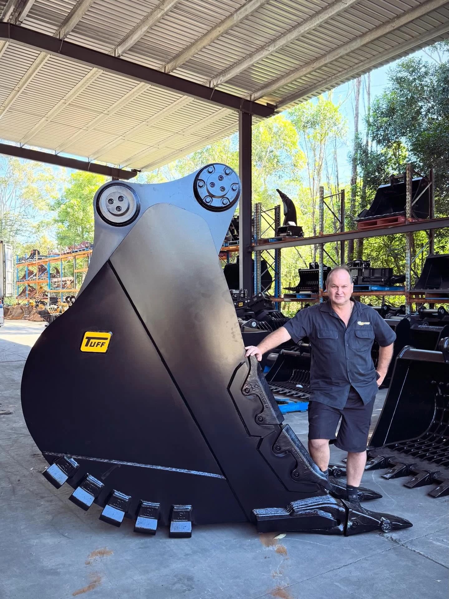 Mick standing beside a large black digger bucket in the Tuff Buckets yard